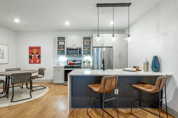 A kitchen with waterfall quartz countertop and glass front cabinets